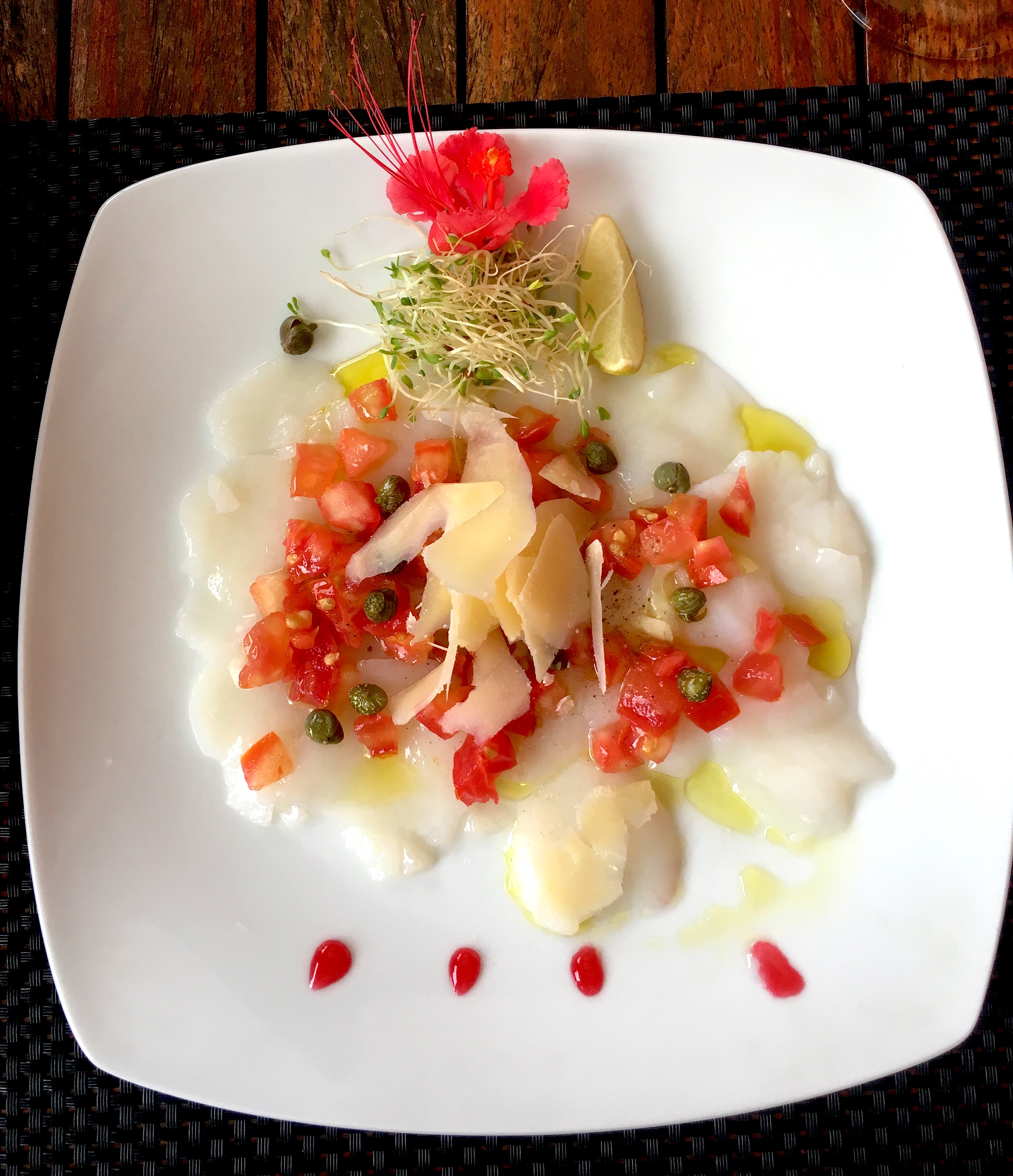 Scallops carpaccio drizzled with olive oil, capers, fresh tomatoes, and shaved parmesan. 
